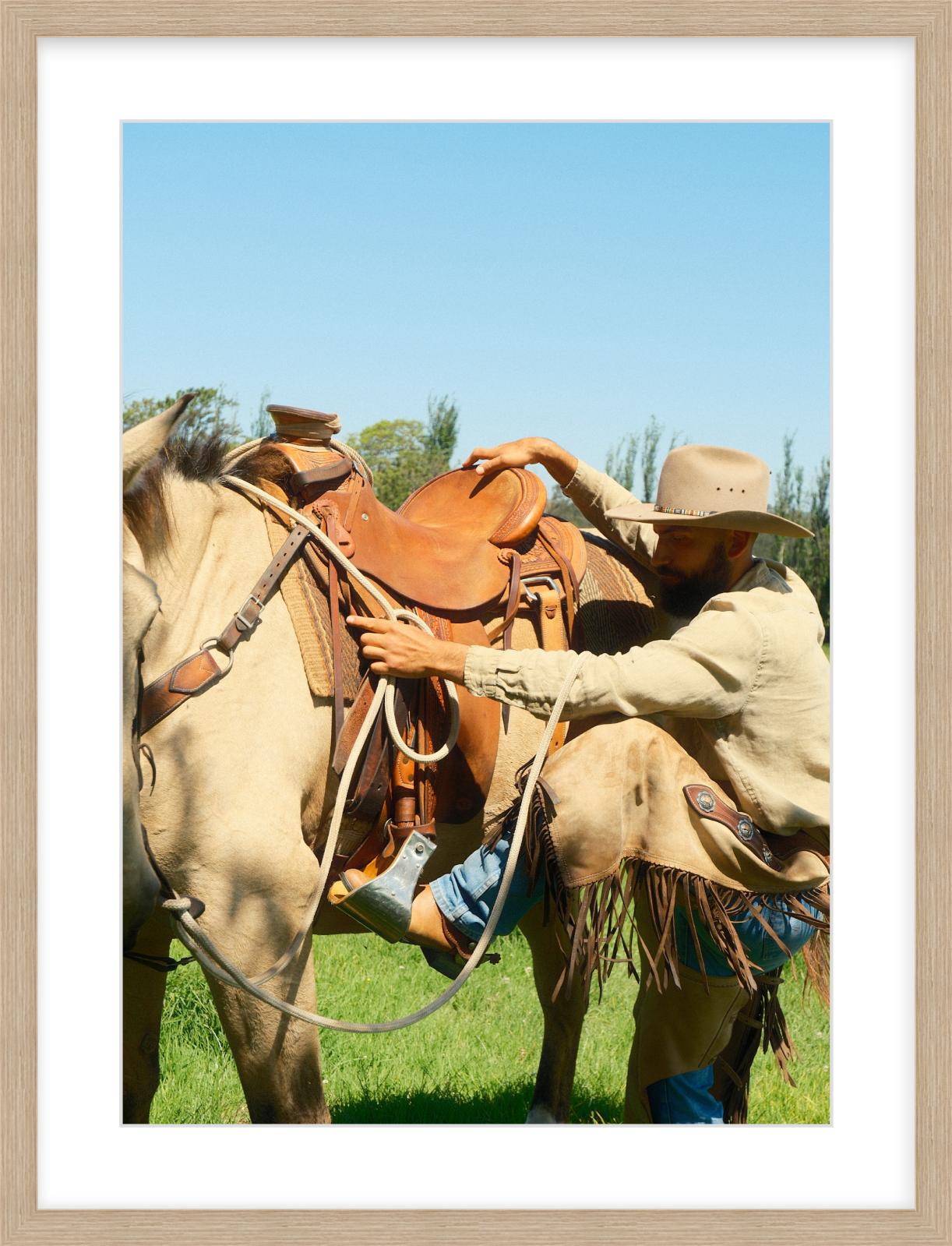 Cowboy adjusting a saddle on a horse with a clear blue sky in the background